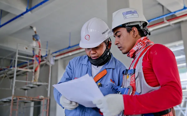 Dos operarios con casco revisando documentacion en obra